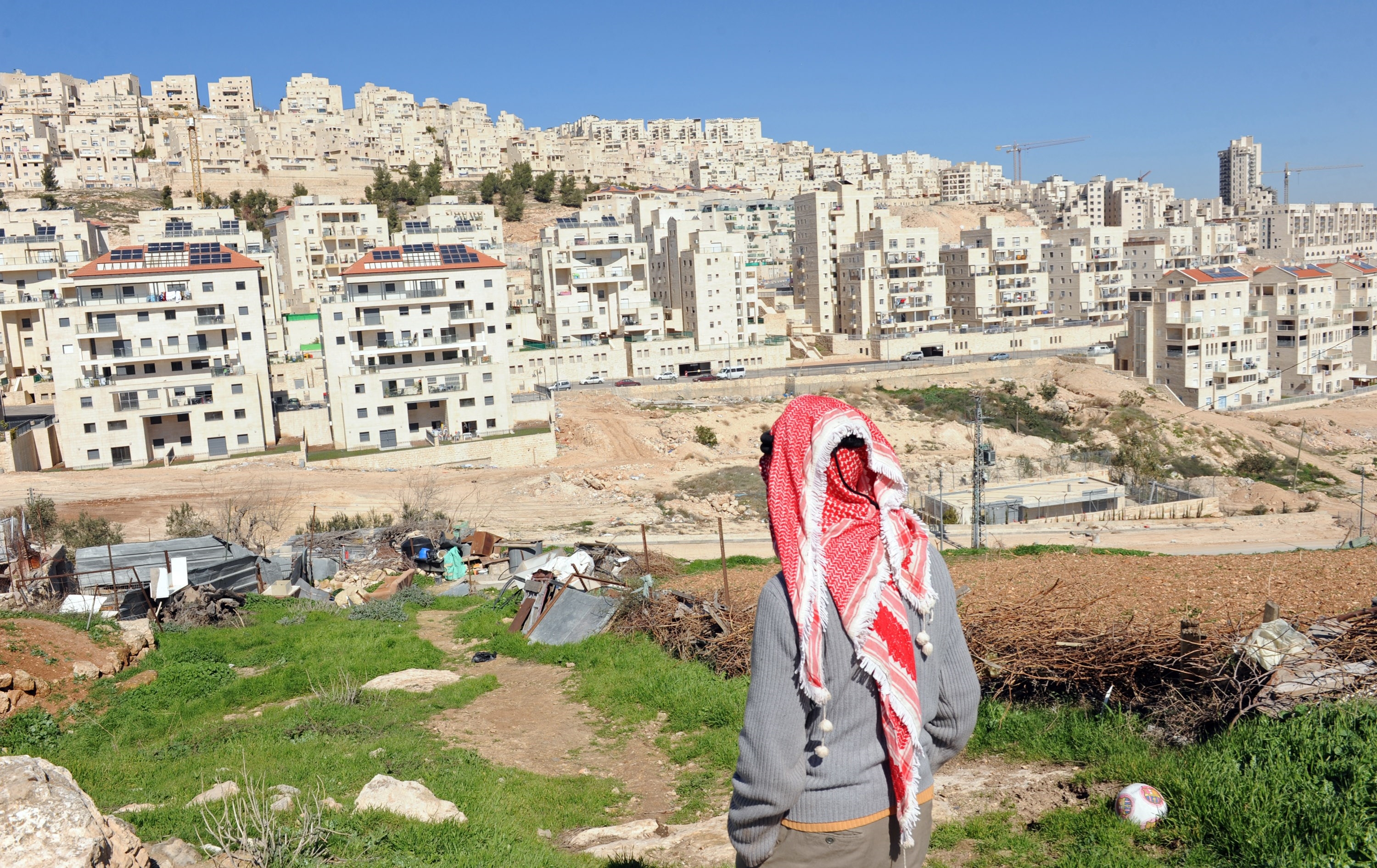 A Palestinian man walks on his property overlooking the Israeli settlement