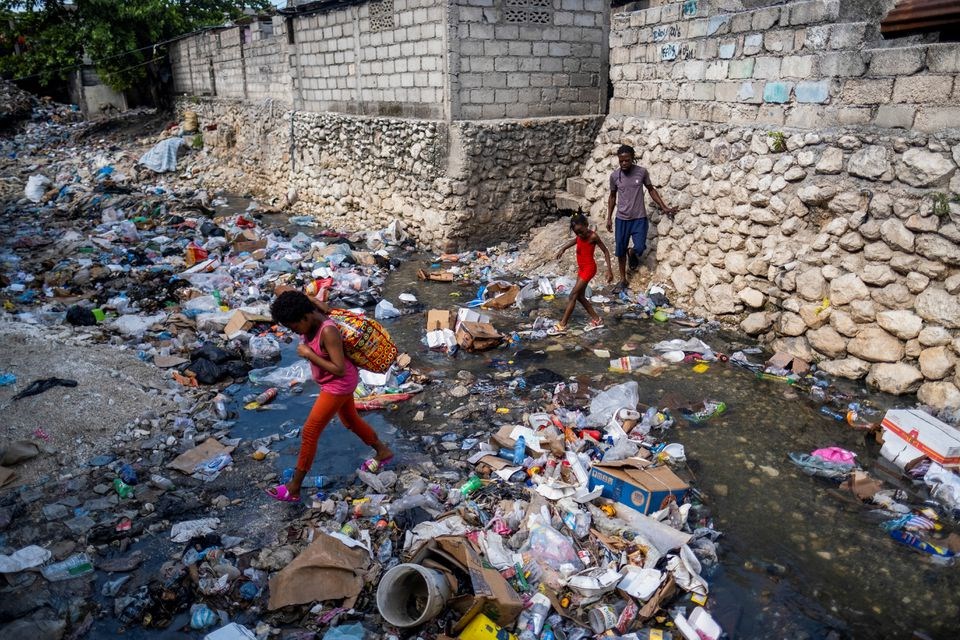 Two girls leap over a stream filled with trash in Port-au-Prince, Haiti October 13, 2022 (Reuters)