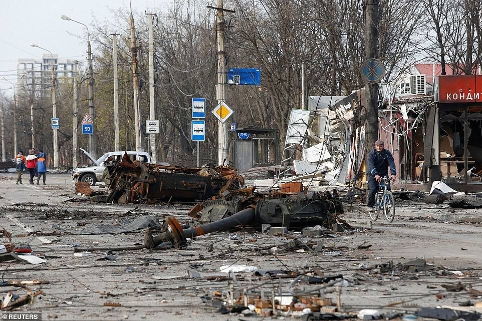 A man cycles past a destroyed tank during the Ukraine-Russia conflict in the southern port city of Mariupol, Ukraine, April 17, 2022. (Reuters)