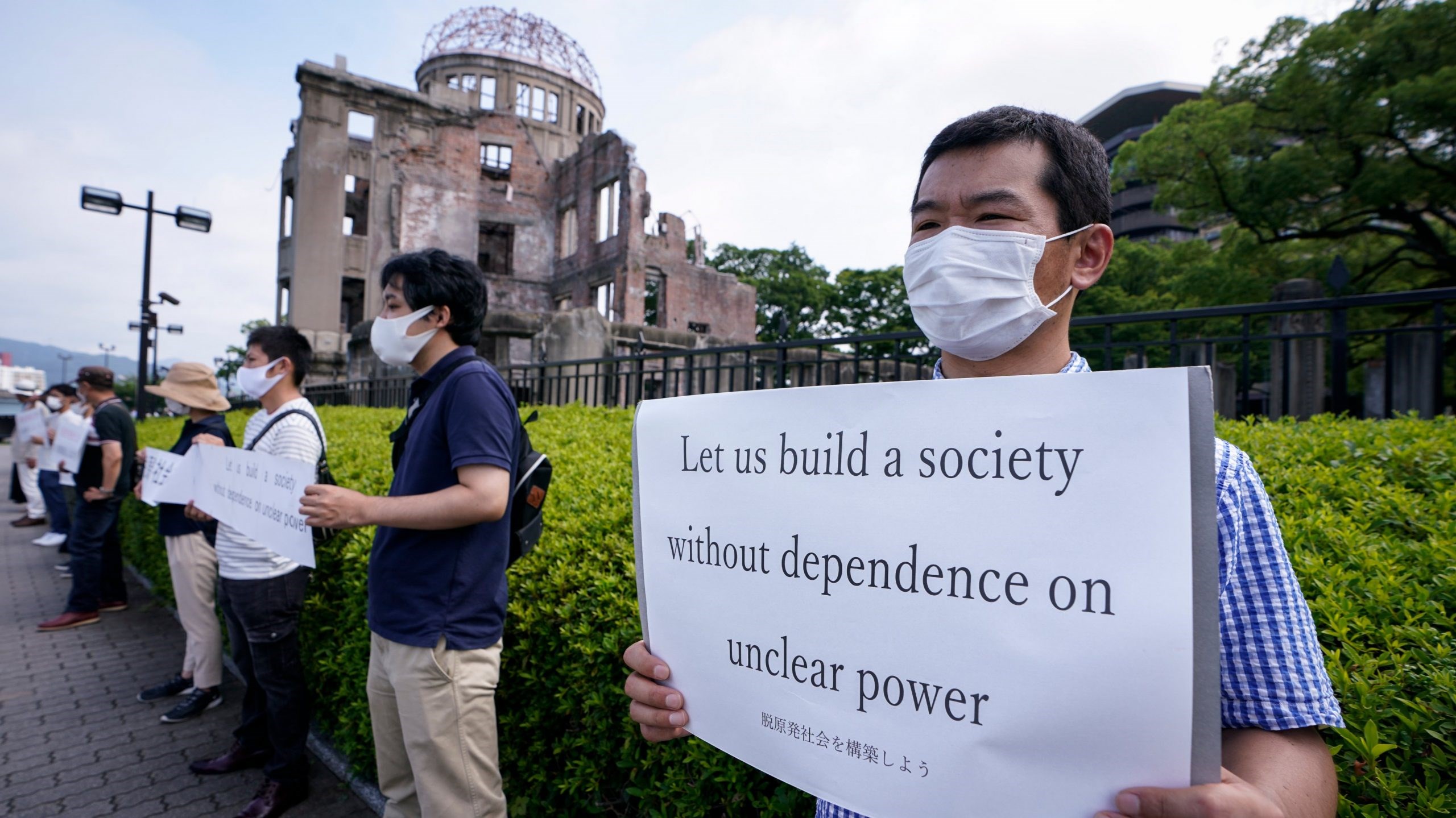 An anti-nuclear power demonstrator holds a placard in front of the Atomic Bomb Dome in Hiroshima, 6 August, 2020 (EPA)