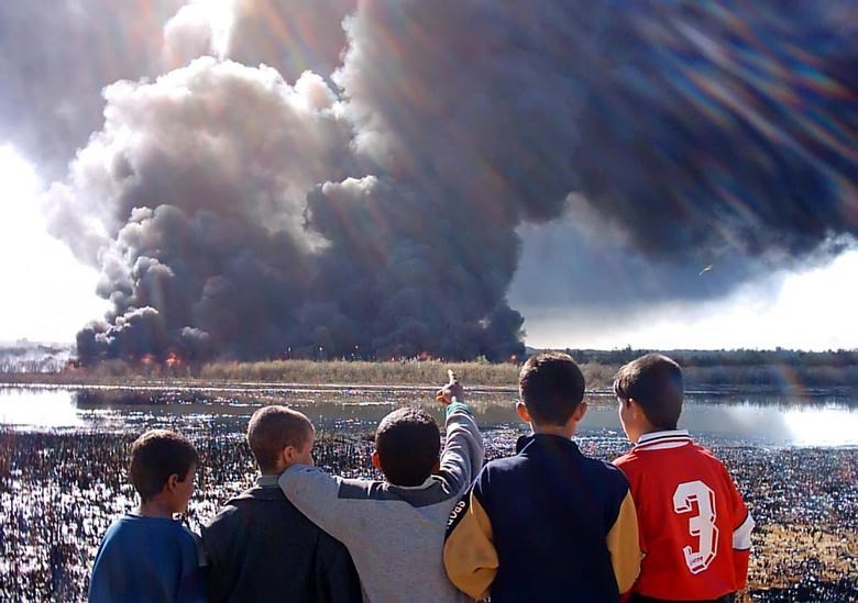 A group of Iraqi boys gather to watch smoke billowing from burning oil on the outskirts of the town of Baiji, north of Baghdad, March 15, 2005 (Reuters)