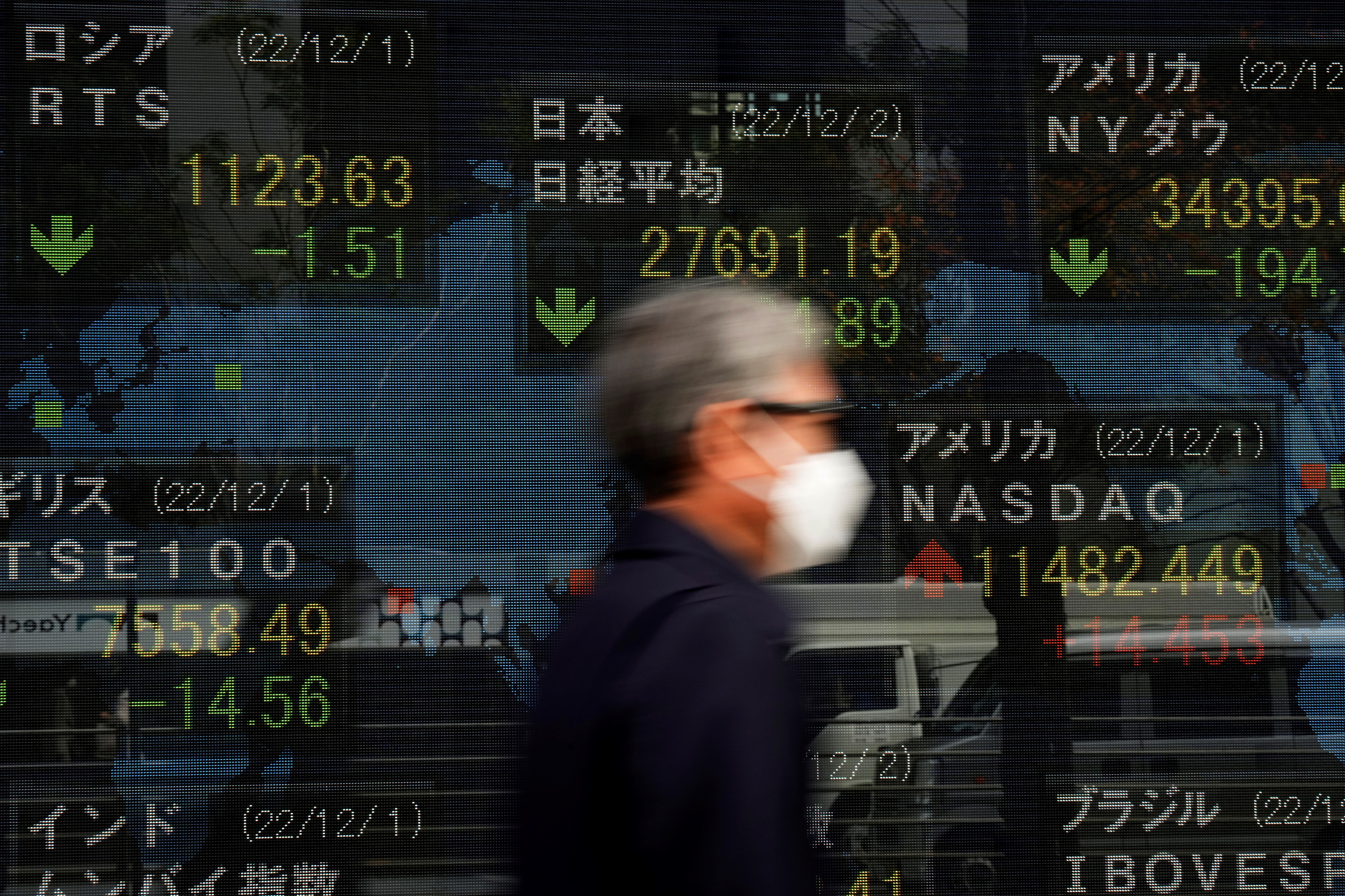 A man walks by monitors showing Japan's Nikkei 225 index and other countries' stock market indexes at a securities firm in Tokyo, Friday, Dec. 2, 2022 (AP Photo/Hiro Komae)