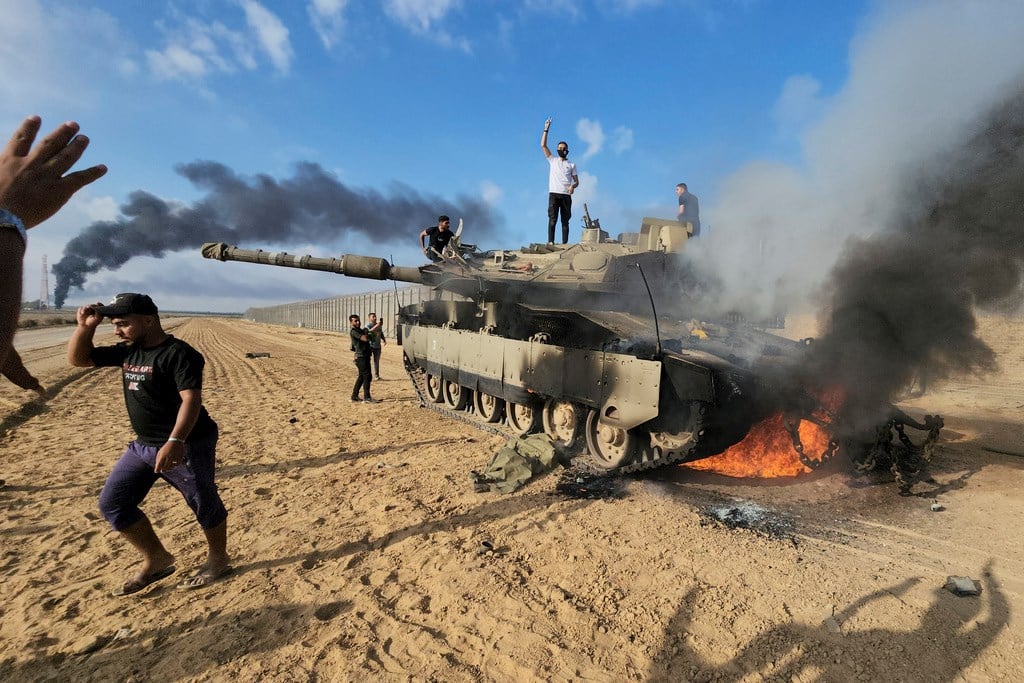 Palestinians celebrate by a destroyed Israeli tank at the Gaza Strip fence east of Khan Younis southern Saturday, Oct. 7, 2023 (AP Photo/Hassan Eslaiah)