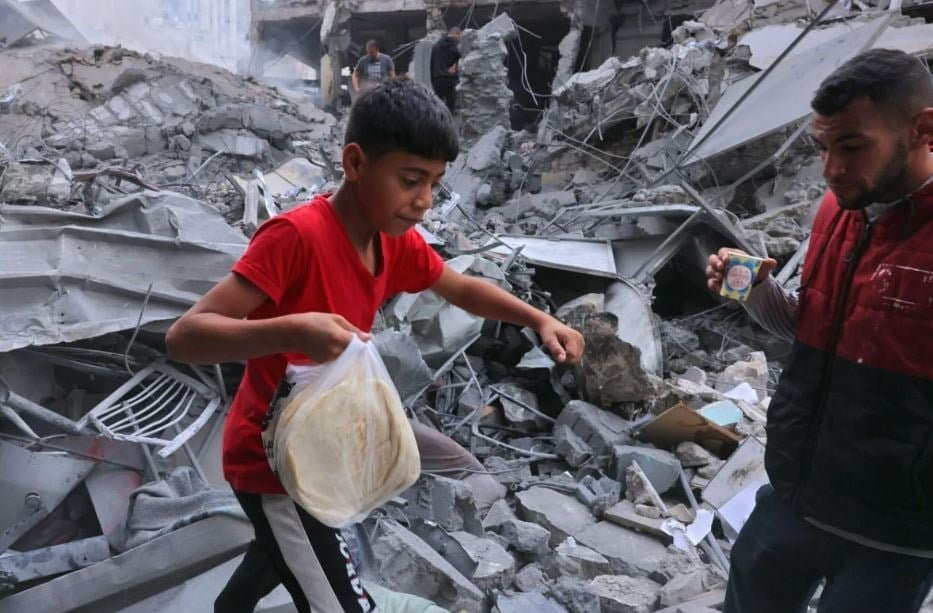 A Palestinian youth carries bread amid the rubble of the city center of Khan Yunis in the southern Gaza Strip following Israeli shelling on October 10. (AFP via Getty Images)