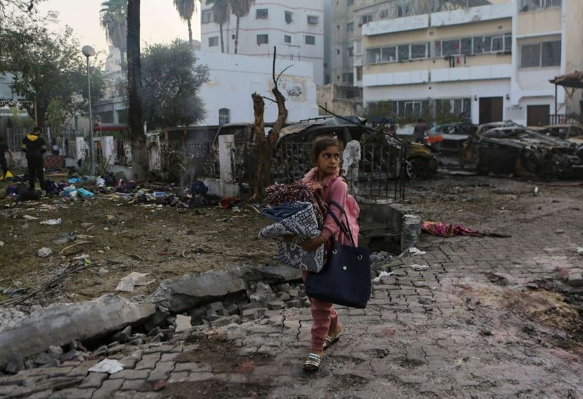 A Palestinian girl carries a blankets as she walks past the site of a deadly Israeli airstrike at Al Ahli hospital, in Gaza City, Oct. 18, 2023. (AP)