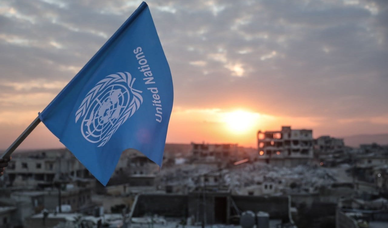 Activists fly an inverted United Nations flag over destroyed buildings in Jindires