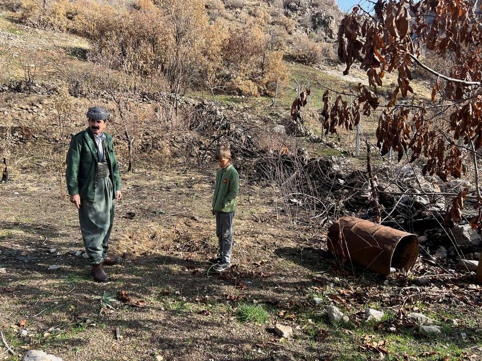 Omar Abdullah Qasim stands with his grandson in the yard next to his house in Sararo village, where he claims several rockets landed during the Turkish bombardment last year, in Dohuk, Iraq, December 27, 2022 (Reuters/Amina Ismail).