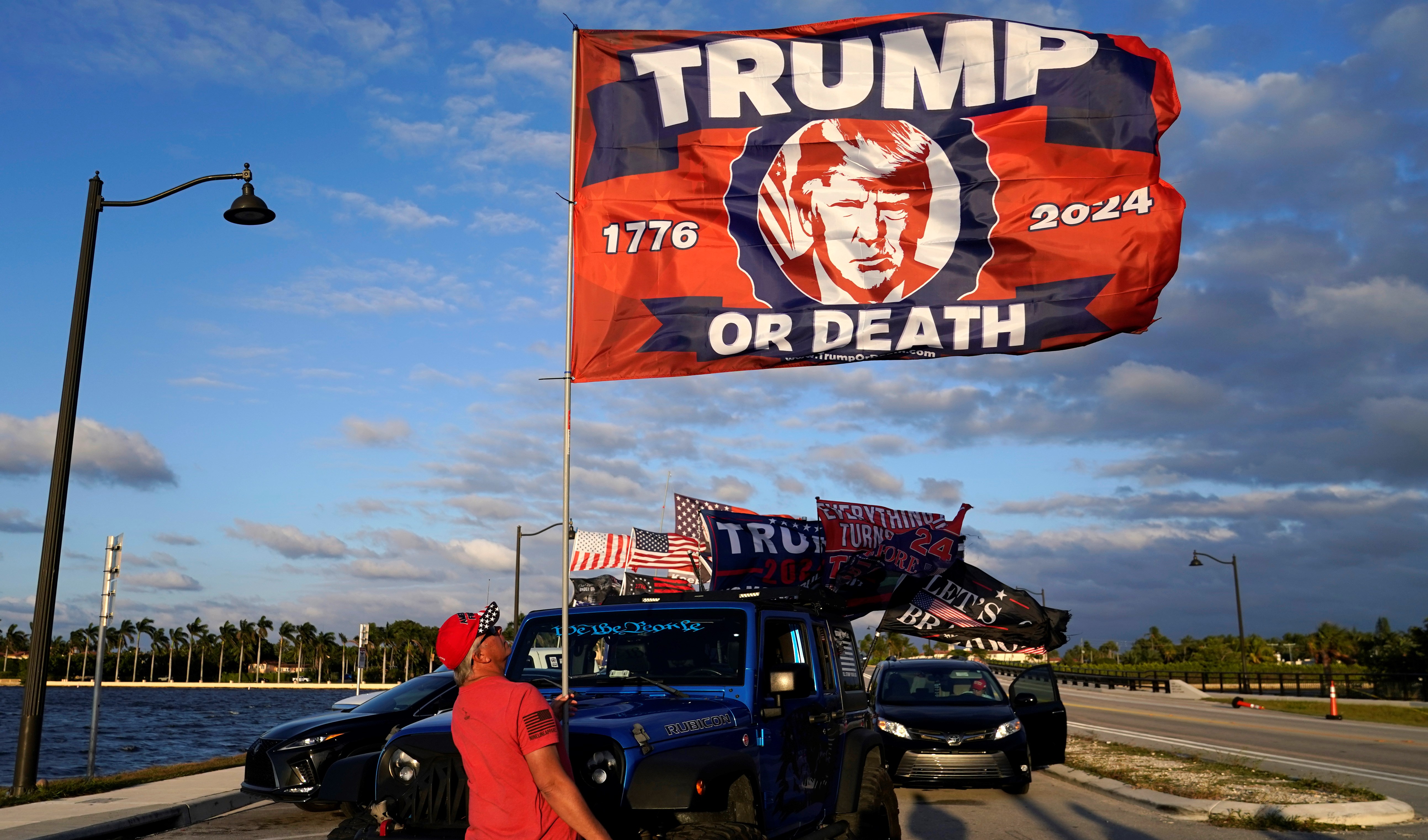 A supporter of former President Donald Trump raises a flag outside of Trump's Mar-a-Lago estate, Monday, March 20, 2023, in Palm Beach, Florida (AP).
