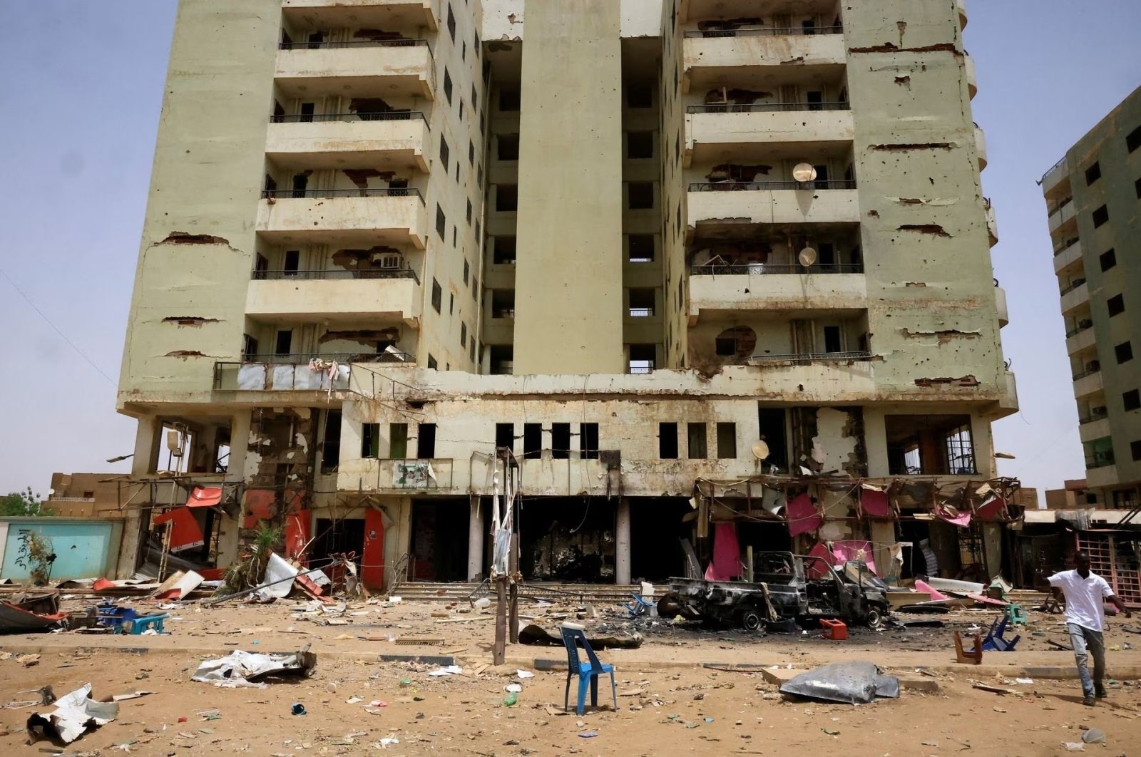 A man walks near a damaged car and buildings at the central market during clashes between the paramilitary Rapid Support Forces and the army, in Khartoum, Sudan, on April 27, 2023 (Reuters)