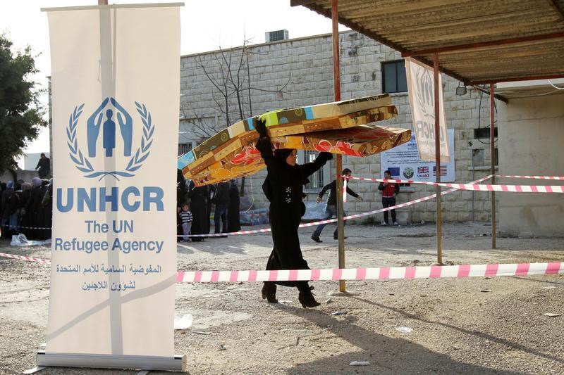 A Syrian refugee carries mattresses as she walks by a banner of the UNHCR at a camp in Batroun, Lebanon, May 13 2015. (Reuters)