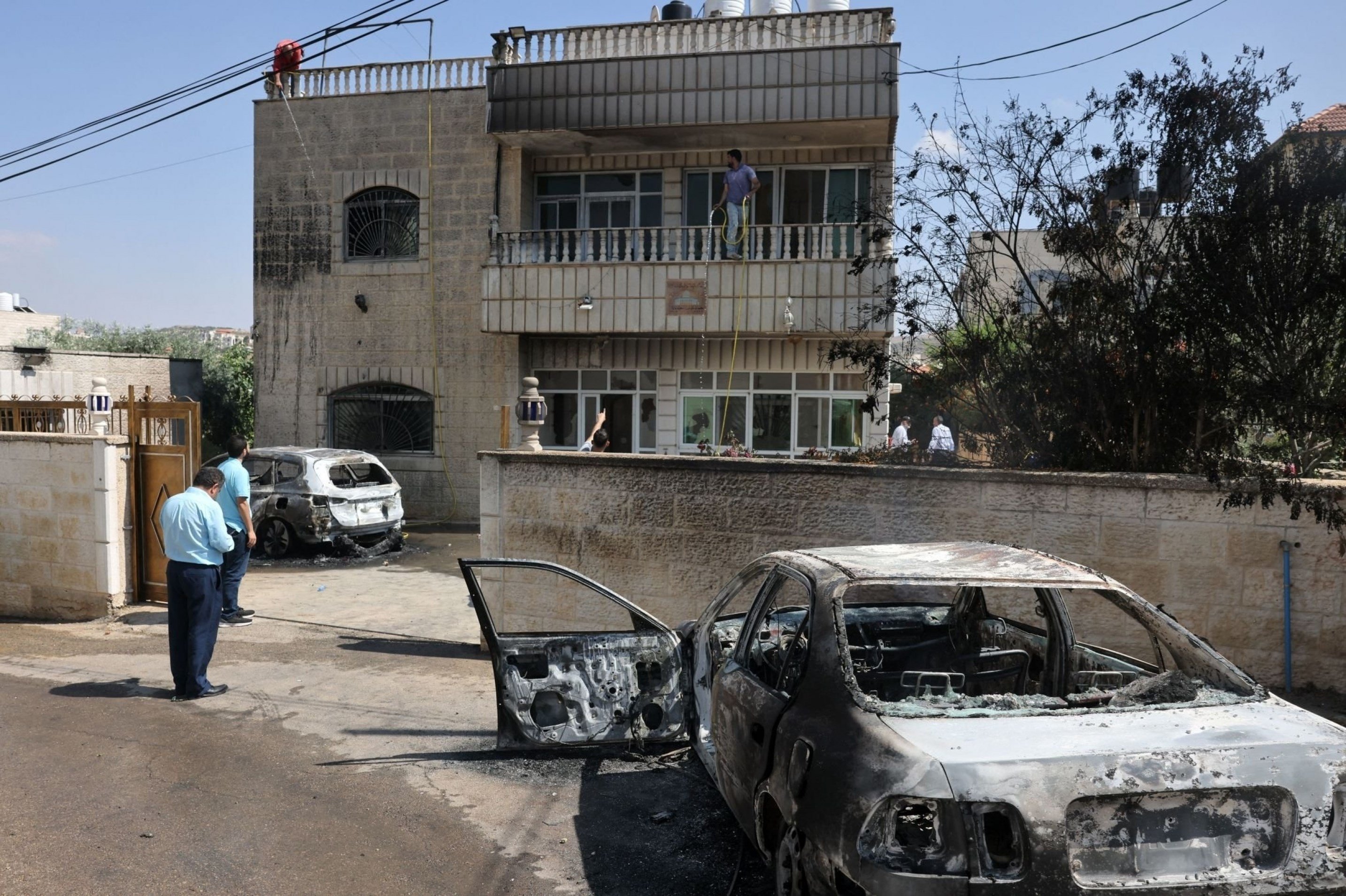 Locals stand by torched vehicles which were set ablaze by settlers who attacked the village of Turmus Aya, occupied West Bank, Palestine, June 21 2023. (AFP)