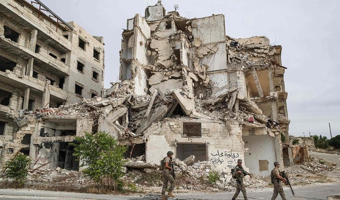 Soldiers patrol along a road past destroyed buildings atop the Arbaeen hill overlooking Ariha in the southern countryside of Syria’s Idlib province. (AFP)