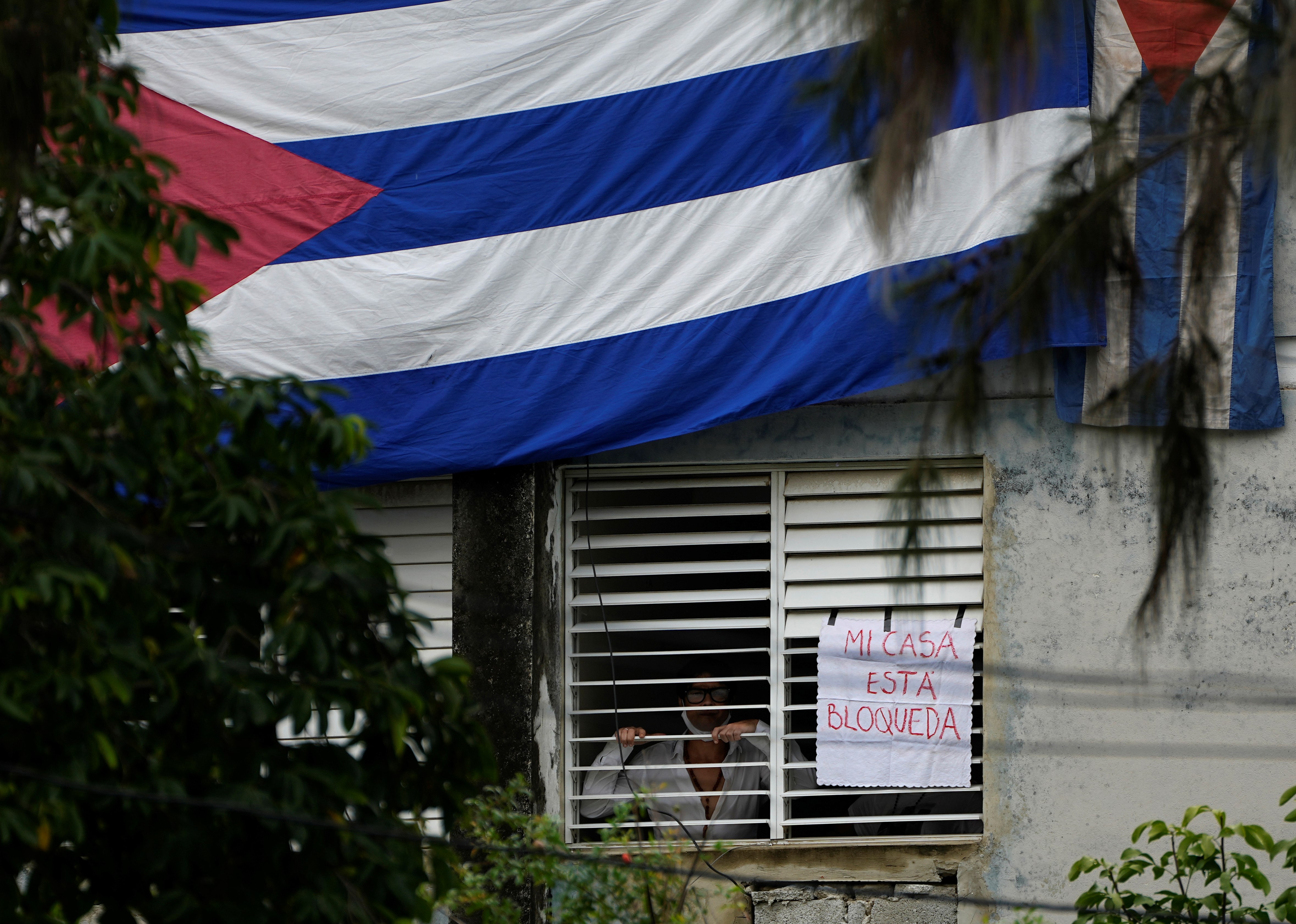 Yunior Garcia, playwright and one of the organizers of a protest march, stands next to a sign that reads in Spanish my house Is blocked, that he posted on a window of his home, in Havana, Cuba, Sunday, Nov. 14, 2021. (AP)