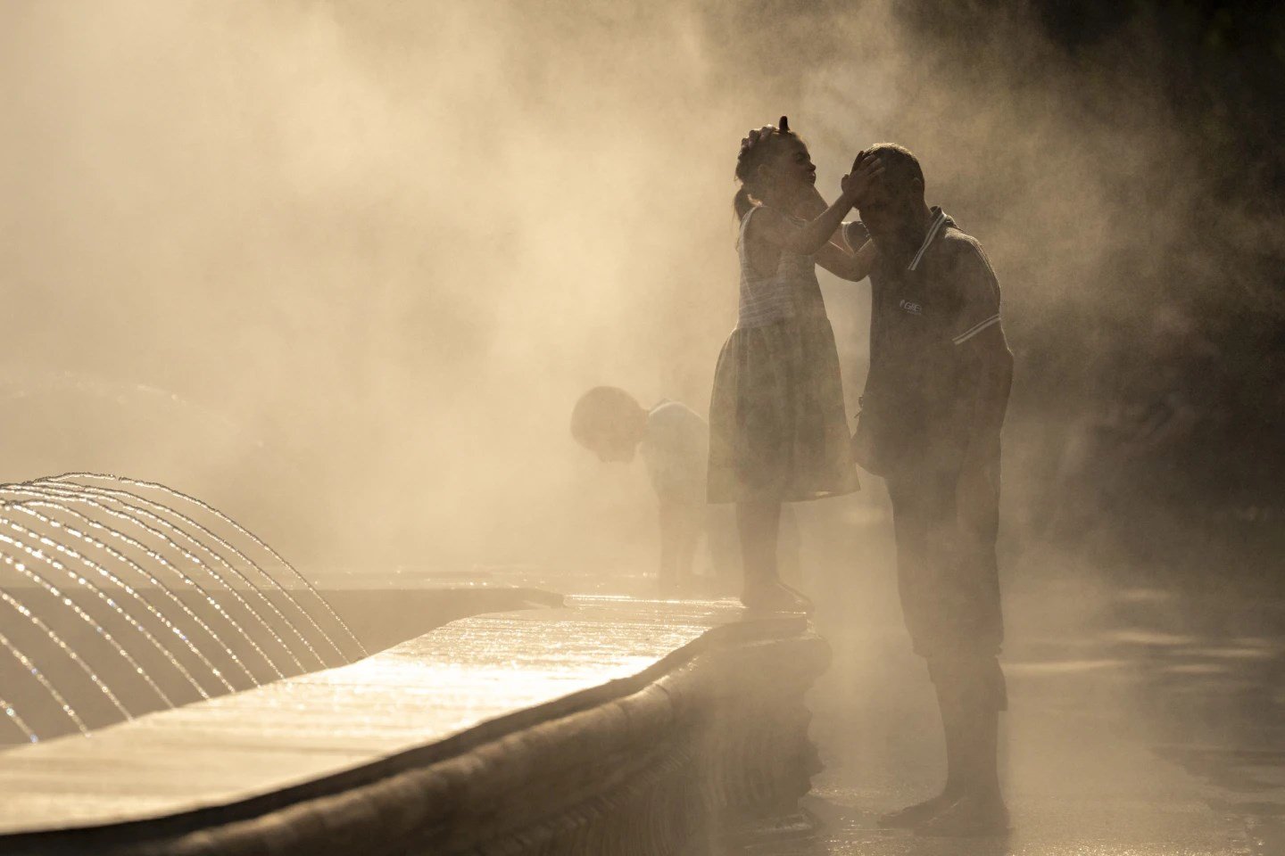 A little girl touches her father’s head as they are engulfed by mist from a public fountain in Bucharest, Romania Thursday, July 13,2023. (AP)