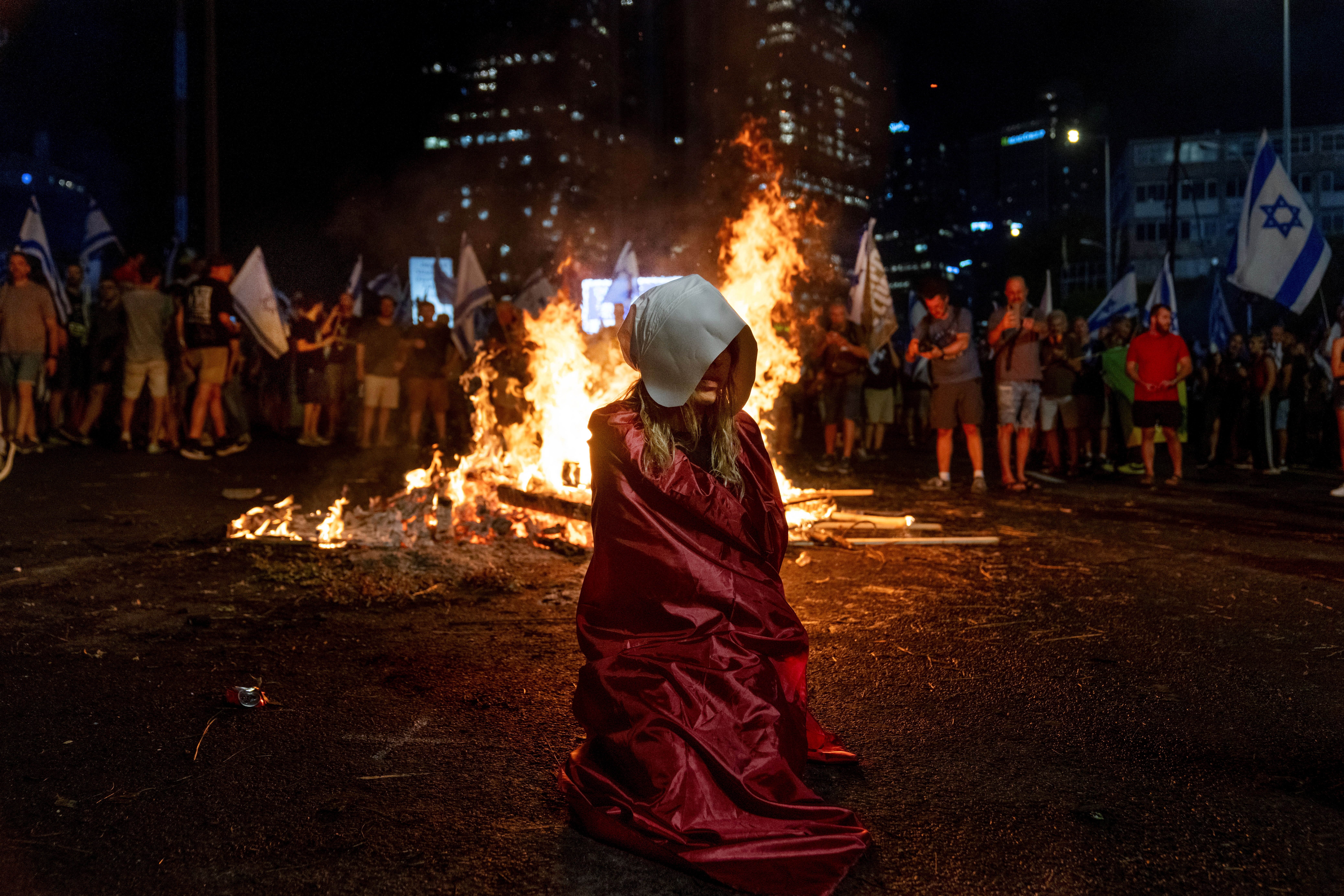 A demonstrator dressed as a character from 'The Handmaid's Tale' TV series and other demonstrators block a highway during a protest in 'Tel Aviv', occupied Palestine, July 5, 2023 (AP)
