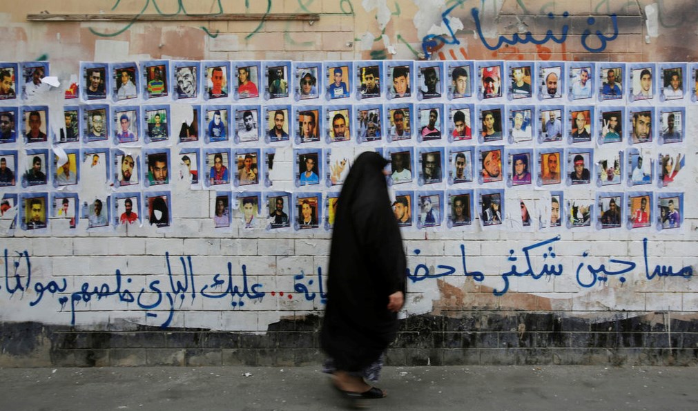 In this Oct. 22, 2015 file photo, a Bahraini woman walks past images of political prisoners plastered on a wall in Sanabis, Bahrain. (AP)