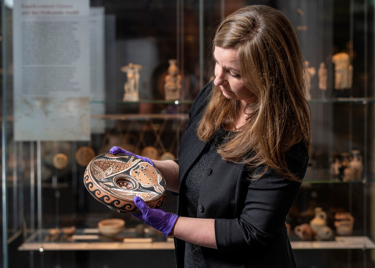 undated handout photo published on September 15, 2023 by the Australian National University (ANU) in Canberra shows ANU Museum curator Georgia Pike-Rowney holding a red Apulian fish plate (AFP)