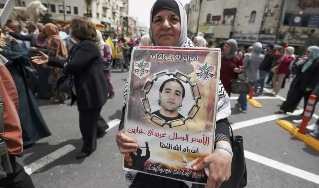 A woman carries a poster bearing the image of a Palestinian prisoner in Israeli prison during a demonstration marking Palestinian Prisoners' Day in Ramallah on 17 April 2022. (AFP)